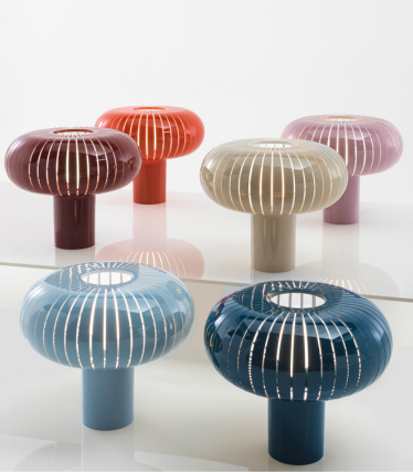 Seis lámparas de mesa decorativas de Kartell en diferentes colores con un diseño estriado en forma de seta sobre una superficie reflectante.