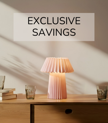 Lámpara de mesa rosa pálido sobre un aparador de madera, rodeada de vasos y libros a la cálida luz del sol.