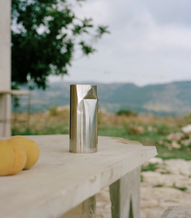 Taza de metal cepillado sobre losa de piedra al aire libre, suave paisaje de fondo.