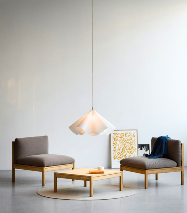 Ligera lámpara colgante sobre sillones bajos en una habitación tranquila y minimalista.