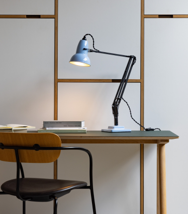 Lámpara de escritorio Anglepoise azul claro sobre una mesa de madera con una silla