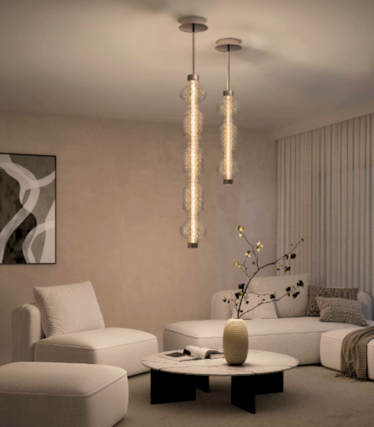Dos esbeltas lámparas colgantes de cristal sobre una mesa de centro de mármol en un salón luminoso con sofá blanco y sillón.