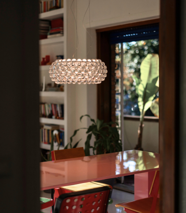 Lámpara colgante esférica de globos de cristal sobre una mesa de comedor roja, vista a través de una puerta.