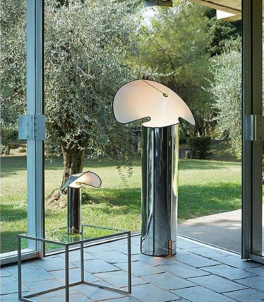 Dos lámparas de pie brillantes con pantallas curvadas en forma de hoja frente a una ventana con vistas al jardín.