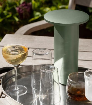 Mesa auxiliar/enfriador cilíndrico verde salvia en una bandeja con vasos y bebidas al aire libre.