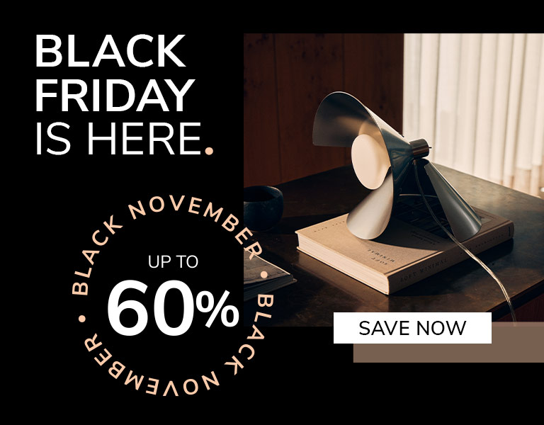 A modern table lamp with angled metal blades sits on top of a book on a dark wooden desk in soft daylight. Text reads: ‘Black Friday is here. Up to 60%. Save Now.’